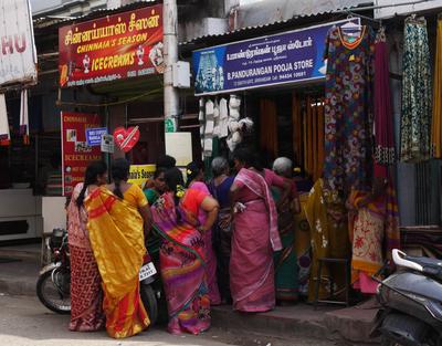 Contrast the lineup for the pooja store with the empty ice cream shop next door.